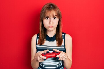 Redhead young woman playing video game holding controller puffing cheeks with funny face. mouth...