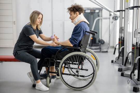 Rehabilitation specialist helps a guy to do exercises for recovery from injury, who is sitting in a wheelchair with a corset around his neck. Concept of physical therapy for people with disabilities