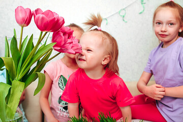 a little girl sniffs pink tulips sisters look at it and smile. A large family of three sisters on the eighth of March holiday