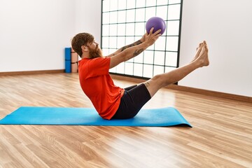 Young redhead man smiling confident training using fit ball at sport center
