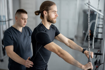 Fototapeta na wymiar Man doing exercises on decompression simulators with the help of rehabilitation specialist. Concept of physical therapy for health and recovery. Idea of kinesiology in the treatment of back
