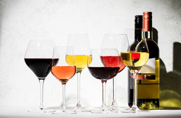 Red, rose and white wine glasses set on gray table background. Wine tasting. Hard light and harsh shadows