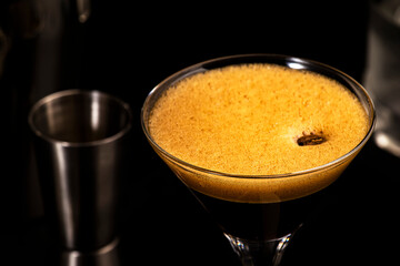 Espresso martini cocktail with vodka, coffee liqueur, syrup and ice, dark bar counter background, bar tools, copy space
