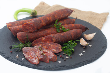 Dry sausages made of pork meat on a black board with fresh herbs and spices.  Smoked, homemade sausage on white background.