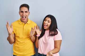 Fototapeta premium Young couple standing over isolated background celebrating crazy and amazed for success with arms raised and open eyes screaming excited. winner concept