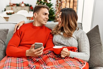 Young couple using smartphone and drinking coffee. Sitting on the sofa at home.