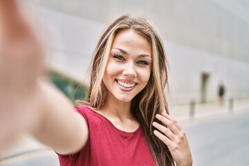 Fototapeta premium Young caucasian girl smiling happy making selfie by the camera at the city.