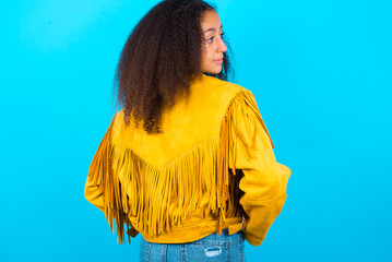 The back view of African teenager girl wearing yellow jacket over blue background Studio Shoot.