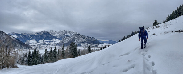 Wanderer mit Rucksack im Schnee mit dem Kaisergebirge im Hintergrund, Tirol, Österreich