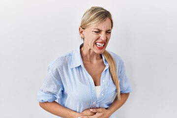 Beautiful blonde woman standing over white background with hand on stomach because indigestion,...