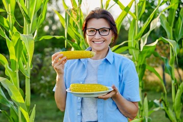 Smiling middle aged woman eating boiled ripe corn on the cob
