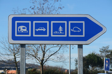Panneau indiquant la direction des parkings pour : caravanes, voitures, bornes de recharge pour véhicules électriques, aire de pique-nique. © Georges Blond