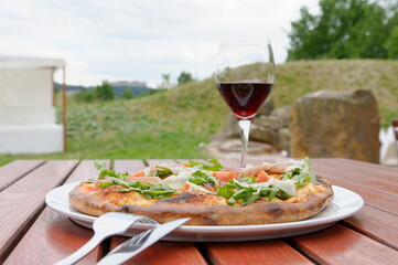 Pizza spezial mit einem Glas Rotwein im Biergarten