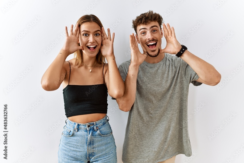 Sticker Young beautiful couple standing together over isolated background smiling cheerful playing peek a boo with hands showing face. surprised and exited