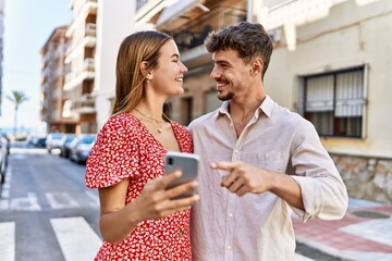 Young hispanic couple smiling happy and using smartphone at the city.