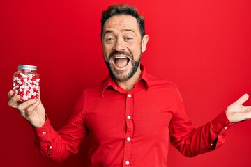 Middle age man holding pills celebrating achievement with happy smile and winner expression with raised hand