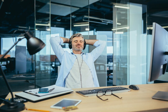 Senior And Experienced Business Man Resting At Work During A Break Listening To Music From Headphones, Manager Working In A Modern Office