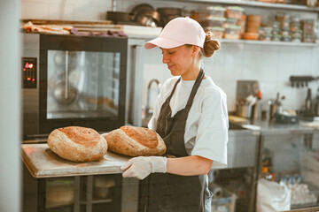 Positive lady holds tray with fresh breads standing in craft bakery workshop