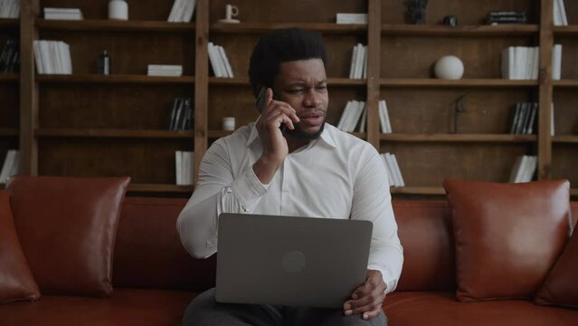 Young adult man recieving bad news on a call while working on his laptop