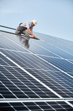Male worker mounting photovoltaic solar panel system outdoors. Man engineer placing solar module on metal rails, wearing construction helmet. Renewable and ecological energy.
