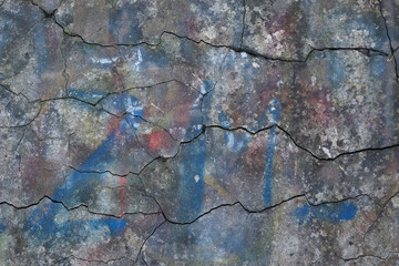 Old cracked beton wall with multicolored paint and graffiti. Rough concrete surface with cracks. Abstract wallpaper, texture or background