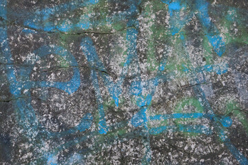 Old cracked concrete wall with bright colorful paint and graffiti. Close-up view of rough cement surface with cracks. Abstract grunge wallpaper, texture or background