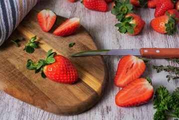 Strawberries on a kitchen cutting board next to a knife on a vintage white wooden background.