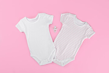 Two white cotton baby bodysuit mockup on pink pastel color background. Empty place for text or logo. Flat lay layout with baby girl clothes, ceramic nipple or baby's dummy, Design bodysuit template