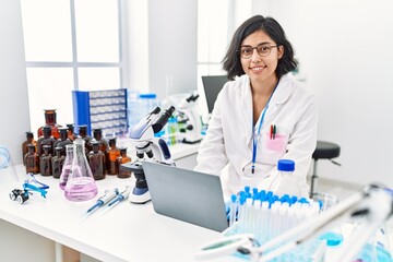 Young latin woman wearing scientist uniform using laptop working at laboratory
