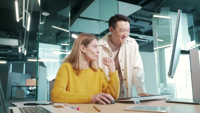 cheerful Crew multiracial team of creative people discussing a project on a computer looking at monitor screen in modern office Two young colleagues in casual asian man and woman point finger teamwork