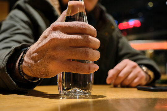 A glass of bottle of water, bottle of water hanging by a man hand. Selective focus photo inside a cafe