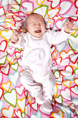 bébé fille caucassien pleurant dans un tissu coloré avec des coeurs roses 