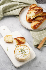 Oven baked camembert cheese with lye baguette bread on marble board, grey concrete surface. Homemade grilled brie with thyme on green checkered kitchen towel
