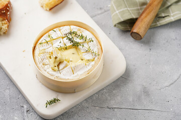 Oven baked camembert cheese with lye baguette bread on marble board, grey concrete surface. Homemade grilled brie with thyme on green checkered kitchen towel