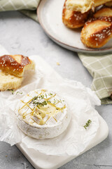 Oven baked camembert cheese with lye baguette bread on marble board, grey concrete surface. Homemade grilled brie with thyme on green checkered kitchen towel