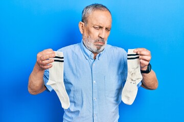 Handsome senior man with beard holding clean andy dirty socks depressed and worry for distress,...