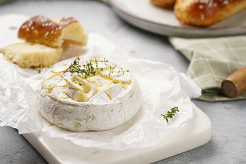 Oven baked camembert cheese with lye baguette bread on marble board, grey concrete surface. Homemade grilled brie with thyme on green checkered kitchen towel - obrazy, fototapety, plakaty