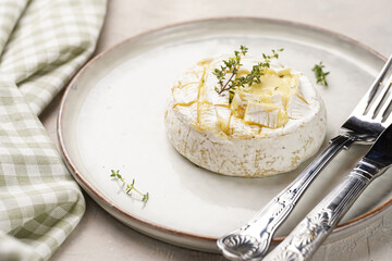 Oven baked camembert cheese with lye baguette bread on white plate, grey concrete surface. Homemade...