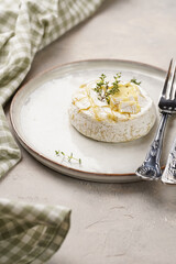 Oven baked camembert cheese with lye baguette bread on white plate, grey concrete surface. Homemade grilled brie with thyme, scandi style table setting