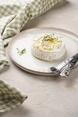 Oven baked camembert cheese with lye baguette bread on white plate, grey concrete surface. Homemade grilled brie with thyme, scandi style table setting