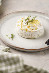 Oven baked camembert cheese on white plate, grey concrete surface. Homemade grilled brie with thyme, scandi style table setting