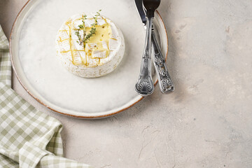 Oven baked camembert cheese on white plate, grey concrete surface. Homemade grilled brie with thyme, scandi style table setting