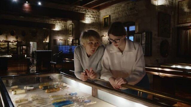 Girl with woman looking with interest at art objects under glass in museum