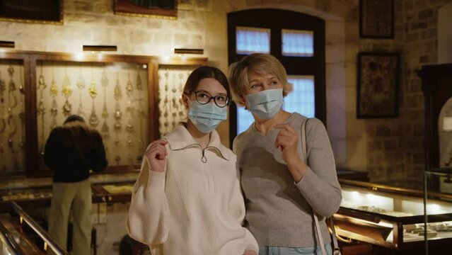 Girl with woman looking with interest at art objects under glass in museum