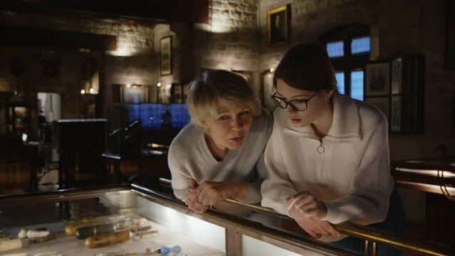 Girl with woman looking with interest at art objects under glass in museum