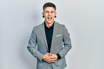 Young caucasian boy with ears dilation wearing business jacket smiling and laughing hard out loud because funny crazy joke with hands on body.
