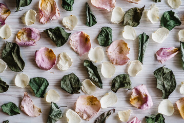 Background with dry rose petals flowers and leaves. Flowers composition made of dried rose on white wooden table. Flat lay, top view, copy space. Place for text and design.