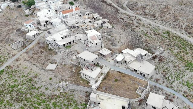 General panorama of small forsaken and destroyed village on hill side, deserted land around. Broken houses with dark windows gaps, only Church stay unbroken