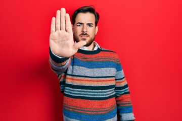 Handsome caucasian man with beard wearing elegant wool winter sweater doing stop sing with palm of the hand. warning expression with negative and serious gesture on the face.