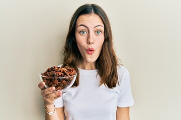 Young brunette woman holding bowl of star anise scared and amazed with open mouth for surprise,...